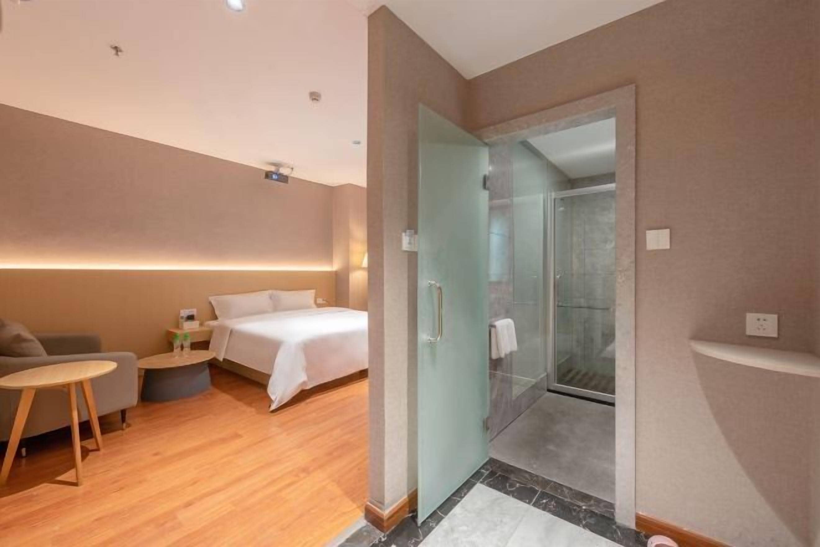 A hotel room with a bed, a small table, a sofa, and a shower area.