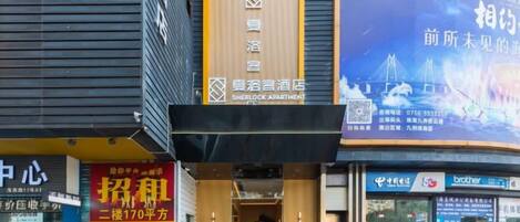 Un hotel con un cartel que indica Sherlock Apartment, una entrada visible y un escaparate con un electrodoméstico de la marca Brother.