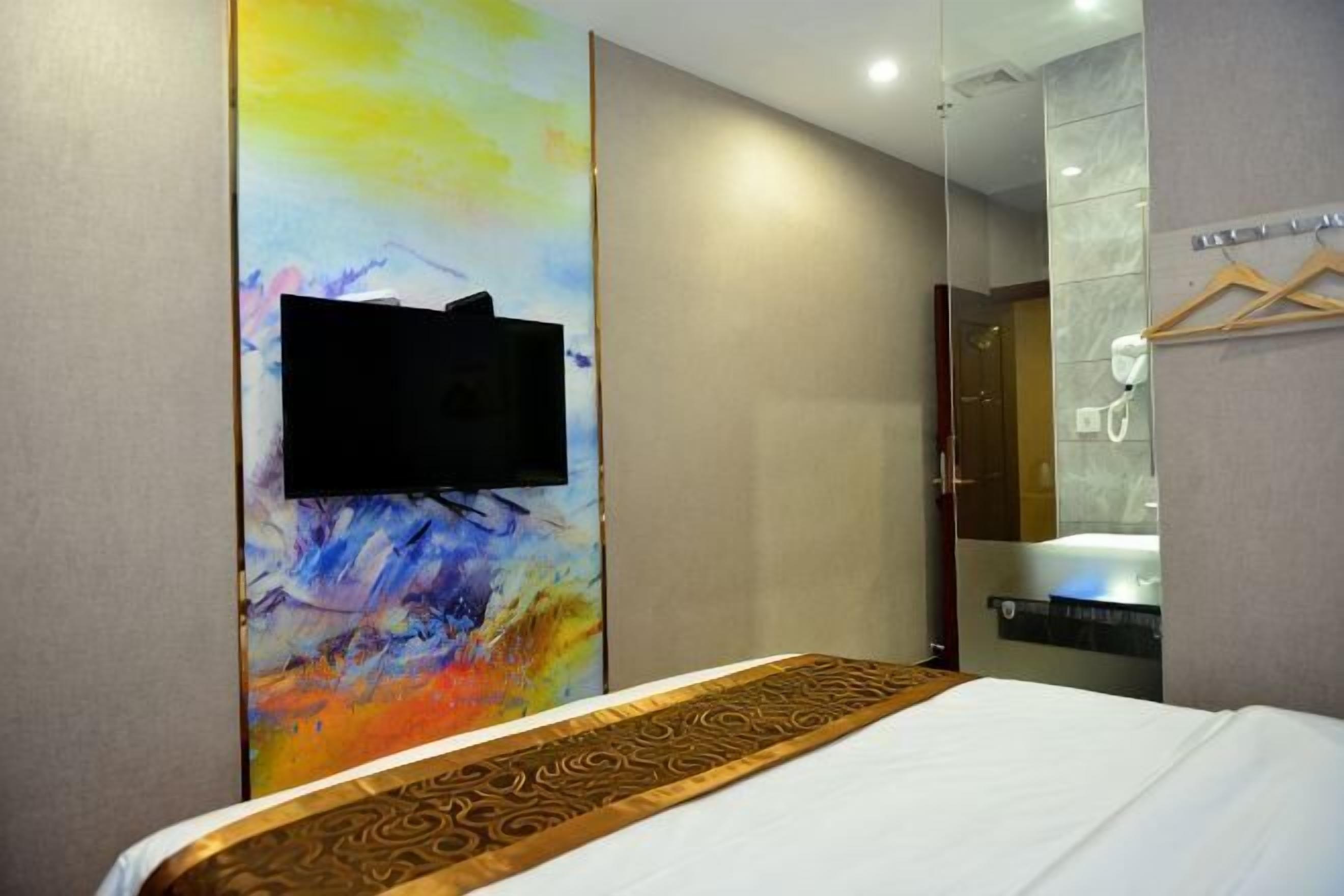 A hotel room with a bed, a television mounted on a colorful wall, and a bathtub.