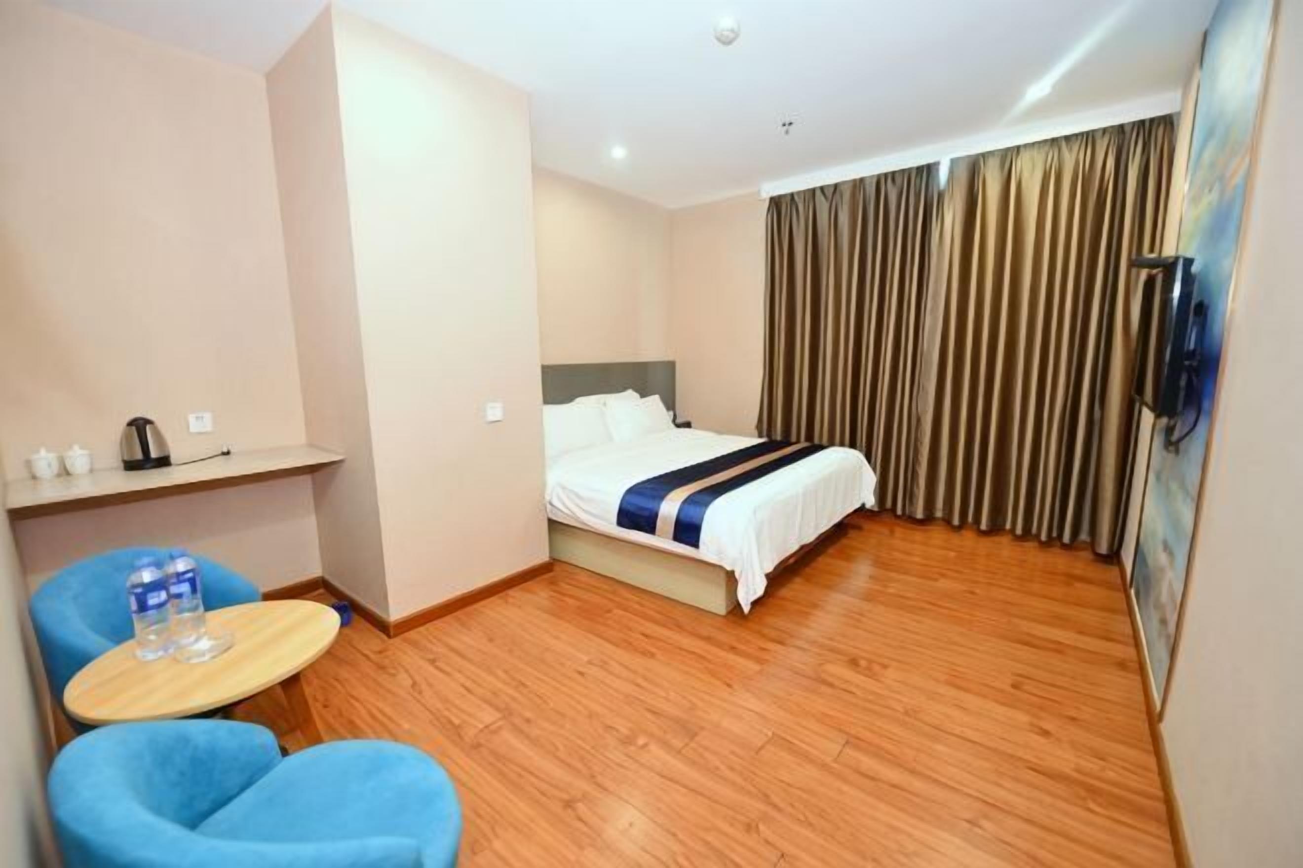 A hotel room with a bed, a small table with a chair, a TV, and a curtain.