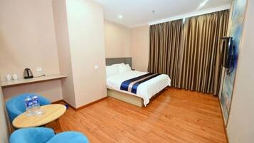 A hotel room with a bed, a small table with a chair, a TV, and a curtain.