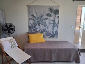 A bedroom with a bed, a fan, a window, and a wall tapestry.
