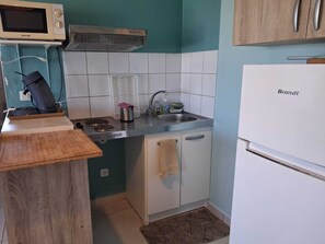 Una cocina compacta con un microondas Brandt, estufa, lavamanos y refrigerador Brandt.