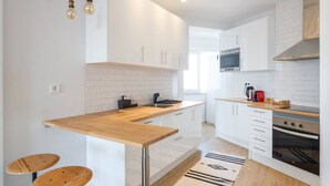 A modern kitchen with white cabinets, a wooden countertop, and a built-in oven. There are two stools and a rug on the floor.