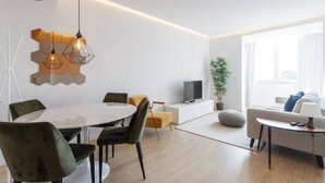 A modern living room with a round dining table, comfortable seating, a flat-screen TV, and a sofa with a lamp.