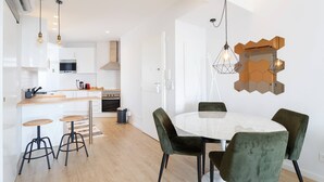 A modern kitchen with white cabinets, a wooden countertop, and a dining area with a round table and green upholstered chairs.