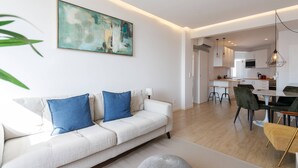 A modern living room with a sofa, a dining area with chairs, and a kitchen in the background.