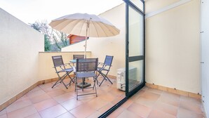 En balkon med et bord, stole og en stor parasol.