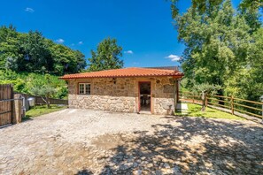 Un edificio in pietra con tetto in tegole rosse, una recinzione in legno e un vialetto sterrato.