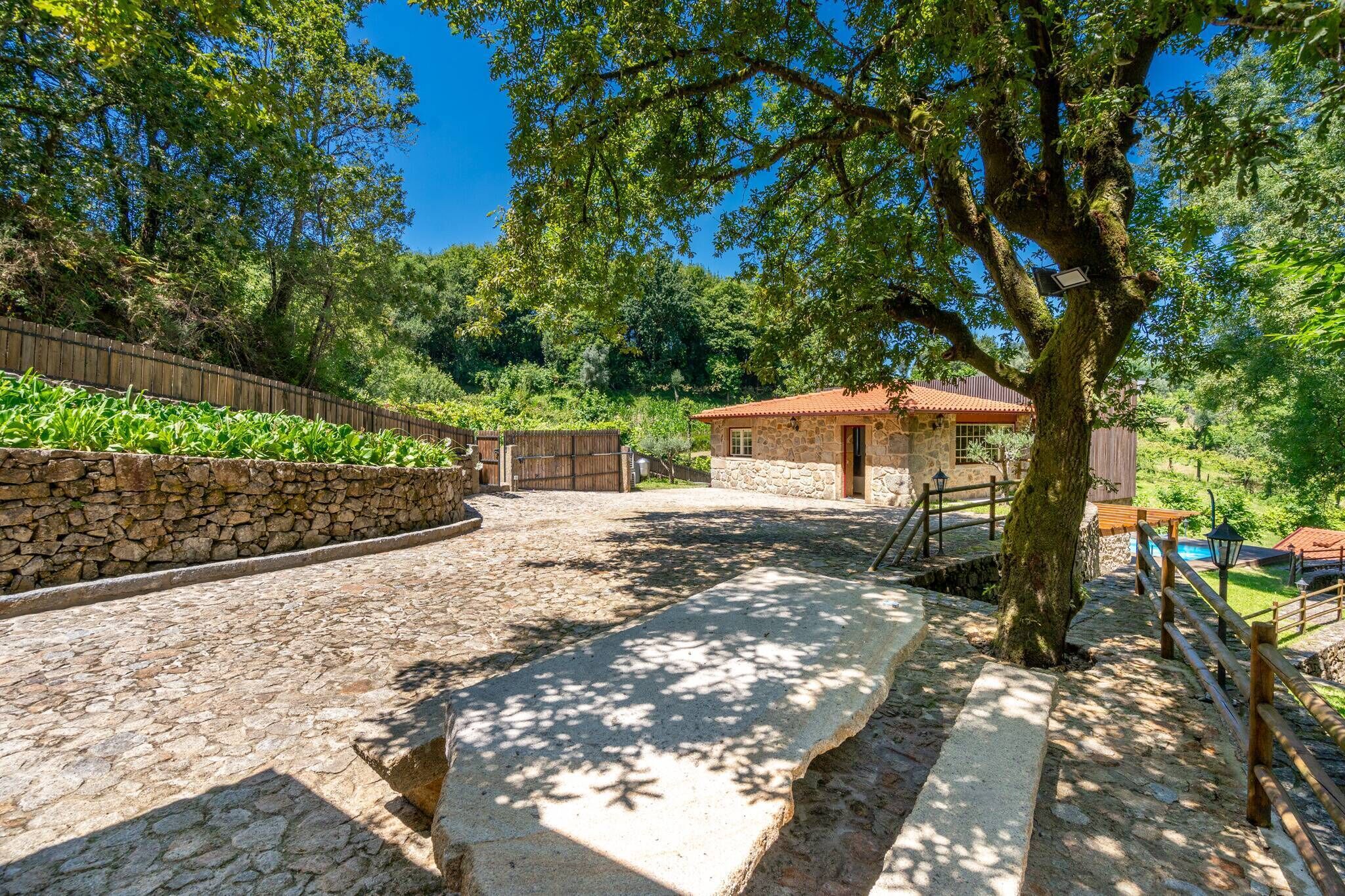 A stone pathway leading to a rustic stone building with a tiled roof, surrounded by lush greenery and trees.