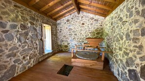 A stone-walled room with a wooden ceiling and a window. - Casa do Penedo - Aqua View (Vila Verde)