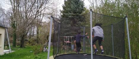 Un trampolín en un patio trasero con red de seguridad, rodeado de árboles y un cobertizo.