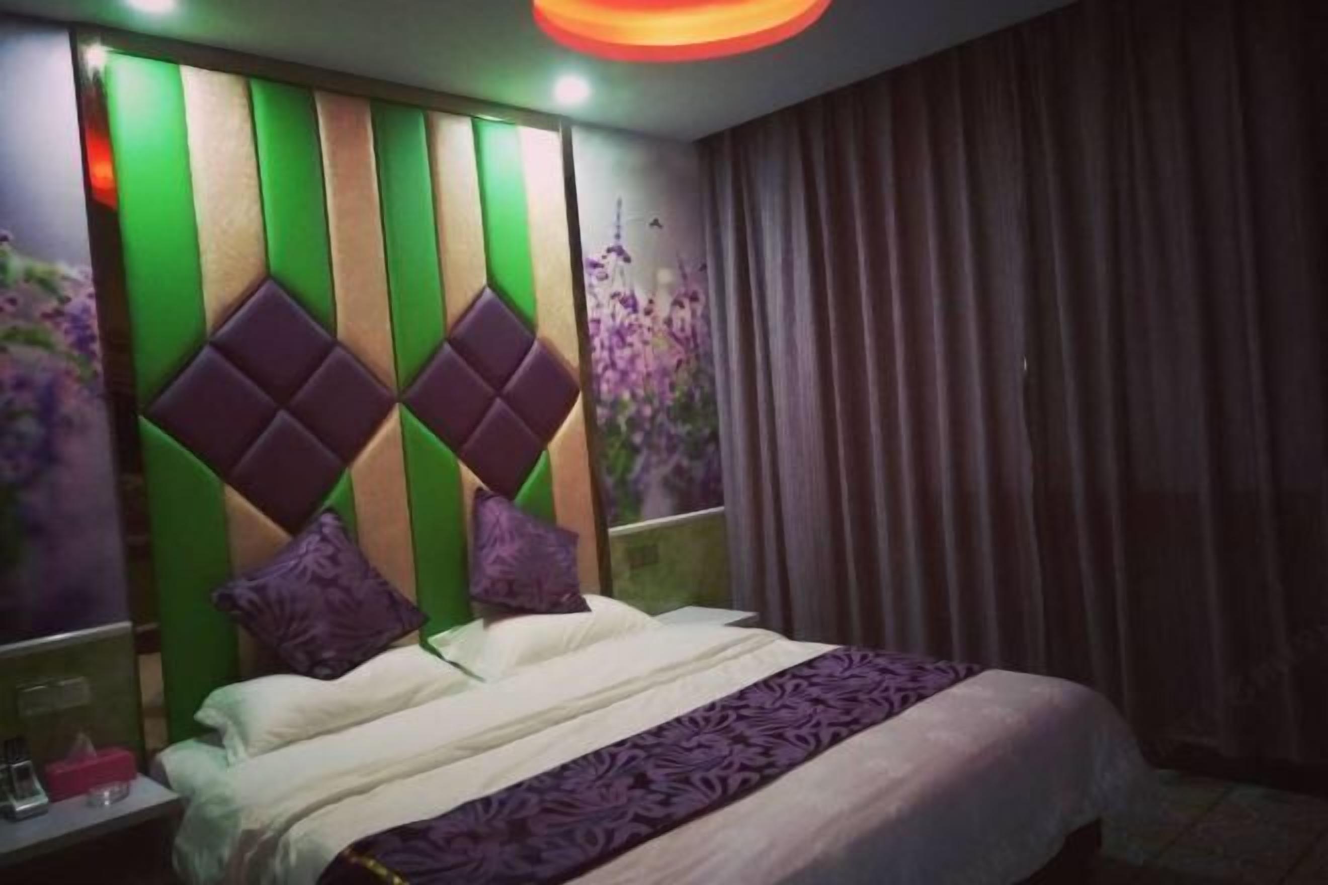Quarto de hotel com uma cama, mesa de cabeceira, parede com painel decorativo e janela com cortinas.