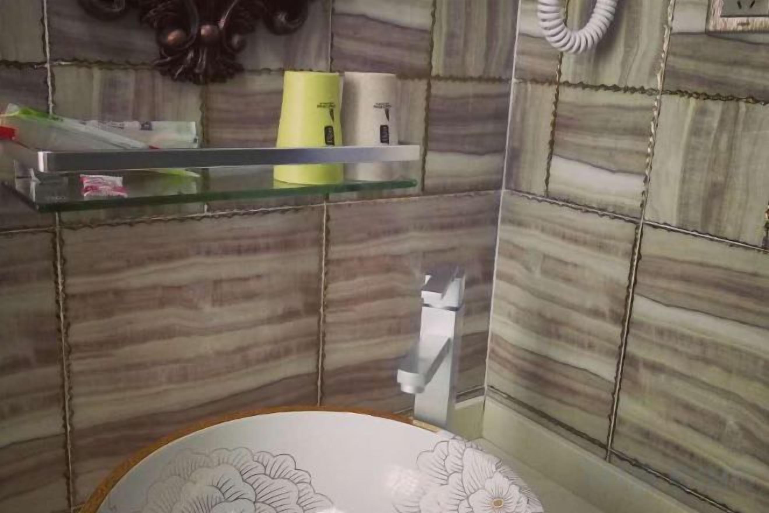A bathroom with a glass shelf holding toiletries, a white sink, and a patterned wall.