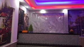 Un'area di accoglienza con un bancone in marmo, parete decorata e luci soffuse colorate.