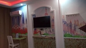 Una stanza con una TV a schermo piatto fissata al muro, un tavolino con una sedia e un murale raffigurante un panorama urbano.