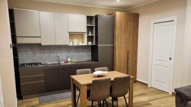 Une cuisine compacte dotée d’appareils électroménagers modernes, un coin repas avec une table et des chaises en bois, et un plancher en bois.