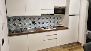 Une cuisine compacte avec des meubles blancs, une cuisinière à gaz, un four à micro-ondes et une plaque de cuisson à deux foyers.