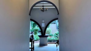 A hallway with a chandelier and an arched doorway leading to an outdoor area with plants. - Hotel Plaza YatBalam (Copan Ruinas)