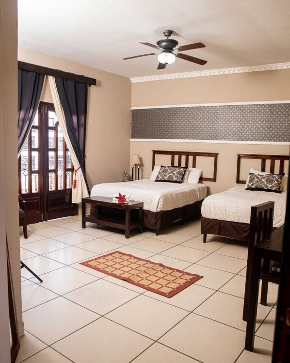 A hotel room with two beds, a ceiling fan, a window with curtains, and a tiled floor.