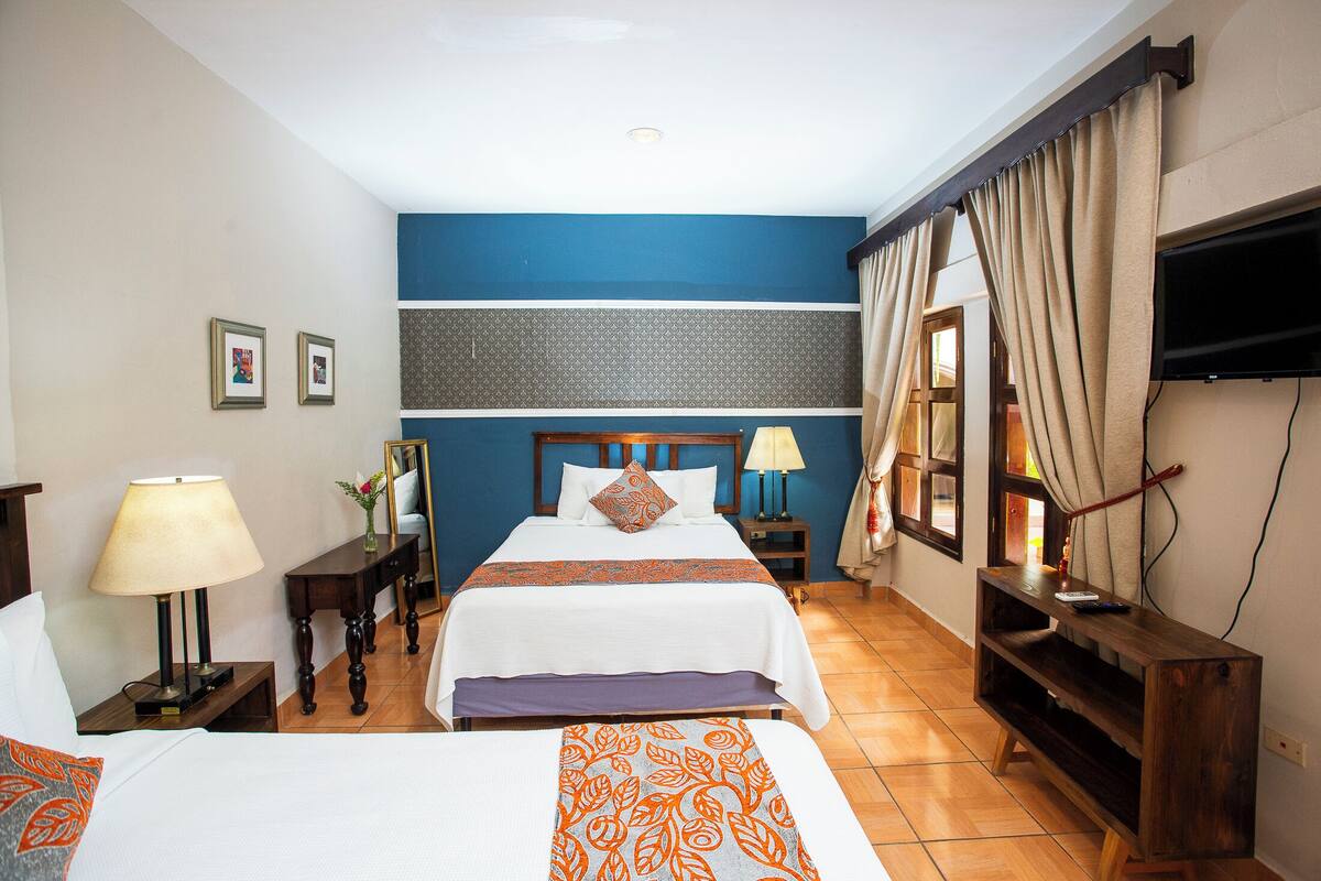 A hotel room with two beds, a TV, a desk, and a window with curtains.