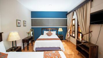 Habitación de hotel con dos camas, televisión, escritorio y ventana con cortinas.