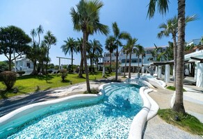 Una piscina con diseño curvo, rodeada de palmeras y un edificio de fachada blanca.