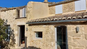 Un bâtiment en pierre avec un toit en tuiles, une cheminée et une fenêtre dotée d’un volet blanc.