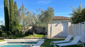 Un jardin avec une piscine, deux chaises longues et un petit bâtiment doté d’un toit en tuiles.