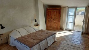 Une chambre à coucher avec un lit, une armoire en bois, une table de chevet avec une lampe, et une vue à travers une porte vitrée.