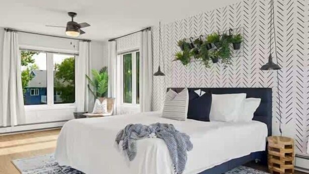 A bedroom with a bed, a ceiling fan, a window with curtains, and a patterned wall.