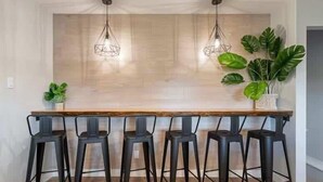 A bar area with a wooden countertop, black stools, and hanging light fixtures.
