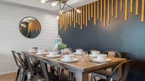 A dining area with a wooden table set for six, black chairs, a round mirror, and a wall-mounted wooden panel design.