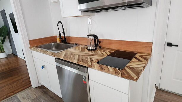 A modern kitchen with white cabinetry, a stainless steel dishwasher, a microwave, and a wooden countertop. - Kenan Cottage in Whirlygig City, Unit B - 3 bd, 2 ba- 1300sf  - Downtown Wilson (Wilson)