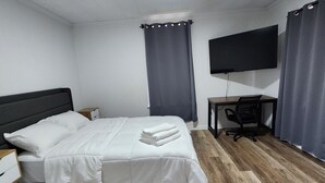 A hotel room with a bed, a desk, a chair, a flat-screen TV, and a ceiling light. - Kenan Cottage in Whirlygig City, Unit B - 3 bd, 2 ba- 1300sf  - Downtown Wilson (Wilson)