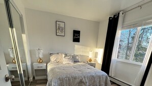 A bedroom with a large bed, bedside tables with lamps, a mirror, and a window with curtains.