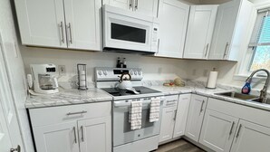 A modern kitchen with white cabinetry, a built-in microwave, a coffee maker, and a kettle.