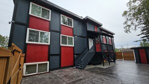 A two-story building with a red and black exterior, a covered patio area, and a wooden fence.