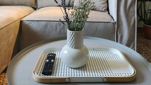A living room with a sofa, a coffee table with a remote control, a vase with flowers, and a floor lamp. - Stylish Athenian Suite Near Acropolis - Balcony • AC • Walk to Everything! (Athens)