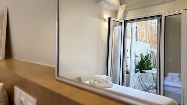 A modern bathroom with a large mirror, a towel rack with neatly folded towels, and a view of an outdoor patio area through the glass door. - Stylish Athenian Suite Near Acropolis - Balcony • AC • Walk to Everything! (Athens)