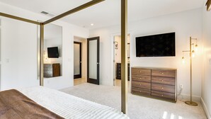 Une chambre à coucher avec un lit à baldaquin, une commode, un téléviseur et une lampe sur pied.