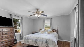 A bedroom with a bed, wooden dresser, ceiling fan, and a TV.