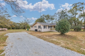 A single-story house with a gravel driveway leading to a front door, surrounded by trees and a clear sky. - Magnolia House - charming 3-bedroom house in Semmes, Alabama (Semmes)