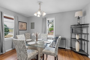 A dining area with a glass table, patterned chairs, a chandelier, and a bookshelf with decorative items. - Magnolia House - charming 3-bedroom house in Semmes, Alabama (Semmes)