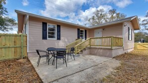 A single-story house with a covered patio area, a small table and chairs, and a wooden fence.