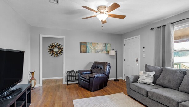A living room with a flat-screen TV, leather chair, gray sofa, and a ceiling fan.