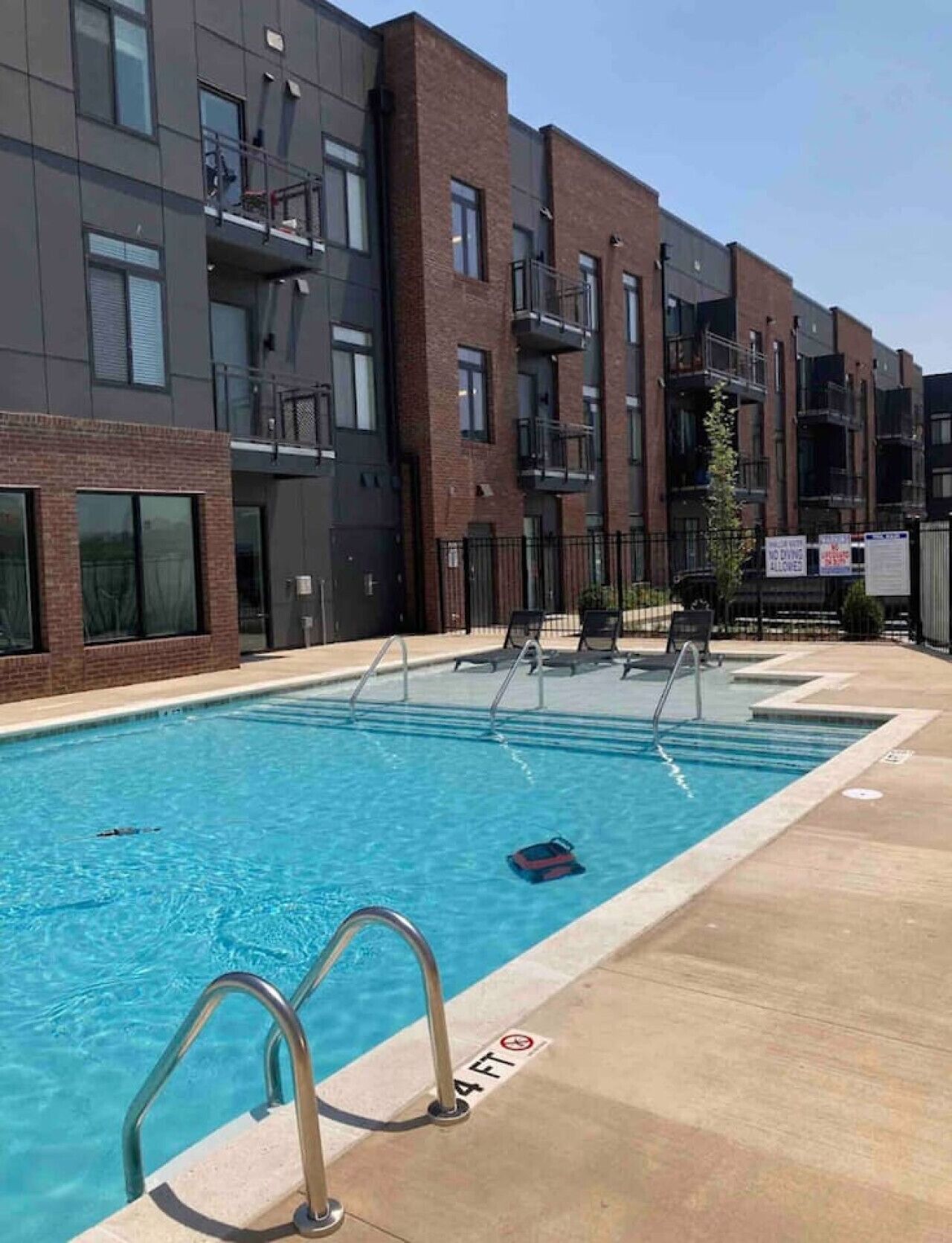 Una piscina con indicador de profundidad de 1,2 metros, rodeada por un moderno edificio de apartamentos con balcones y un cielo despejado.