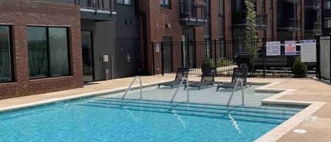 Una piscina con indicador de profundidad de 1,2 metros, rodeada por un moderno edificio de apartamentos con balcones y un cielo despejado.