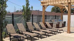 Eine Außenpatio mit vier Liegestühlen, einer Holzpergola und einem Grill.