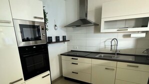 A modern kitchen with white cabinets, a black oven, a stainless steel range hood, a sink, and a countertop. - C&V: 3 PP - 2 rooms +WLAN+Smart-TV+Boxspringbed (Kaiserslautern)